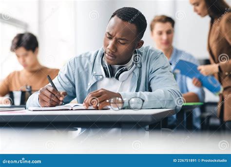 Black Male Student Sitting At Desk In Classroom Writing Exam Stock