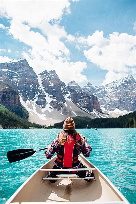 Back View Of A Woman Canoeing In A Vibrant Blue Lake With Mountains In
