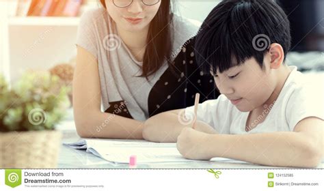 Asian Mother With Son Doing Homework In Living Room Stock Image
