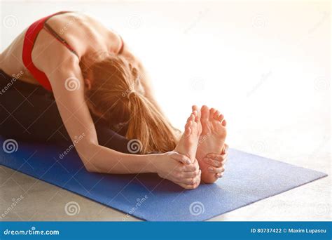 Profile Shot Of Young Woman Stretching To Touch Her Toes While Sitting