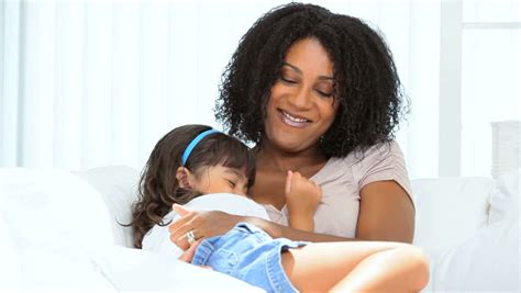 Beautiful Young Ethnic Mother Tickling Her Giggling Pre School Daughter On Home Couch Stock