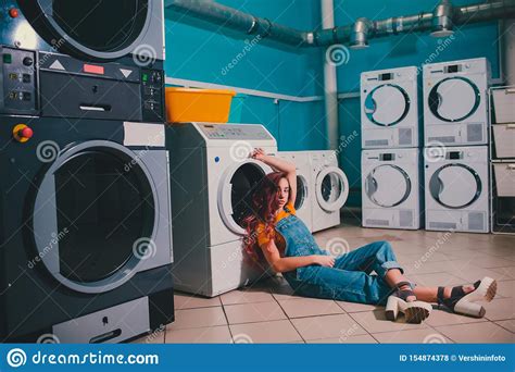 Young Woman Searching Clothes In Washing Machine Drum At Laundromat