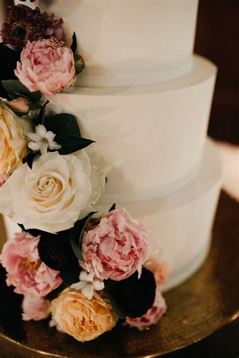 Close Up Of Modern Wedding Cake With Lush Florals Set On A Gold Cake
