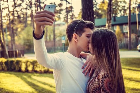 Free Photo Cute Female Kissing Her Boyfriend When He Taking Selfie In A Park
