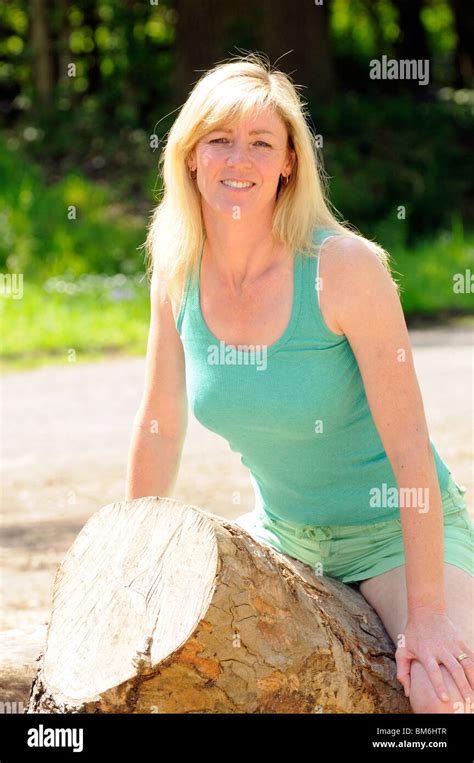 portrait of a mid forties blonde woman outdoors sitting on a felled tree a three quarter body