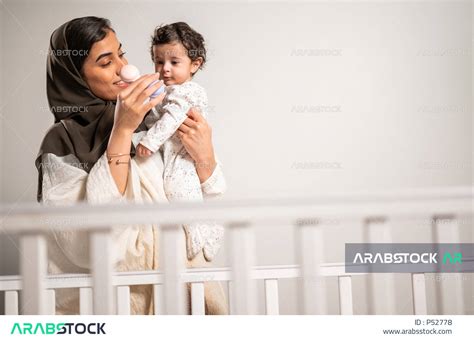 أم عربية خليجية سعودية تحمل طفلها الرضيع بحب وحنان، تلاعب طفلها بلعبة تعليمية للأطفال بإيماءات