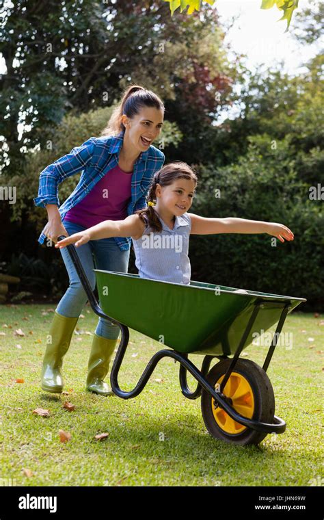 Cheerful Mother Pushing Daughter Sitting In Wheelbarrow At Backyard