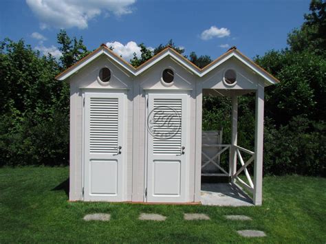 Two White Outhouses With Shutters On Each Side In The Middle Of Green Grass