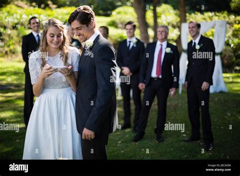 Bride And Groom Reviewing Photographs On Mobile Phone During Wedding