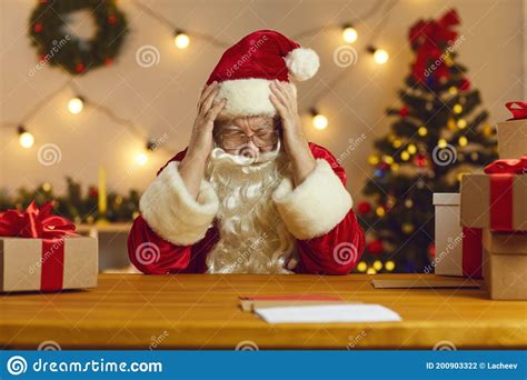 Sad Old Bearded Santa Claus Sitting At A Table Holding His Head