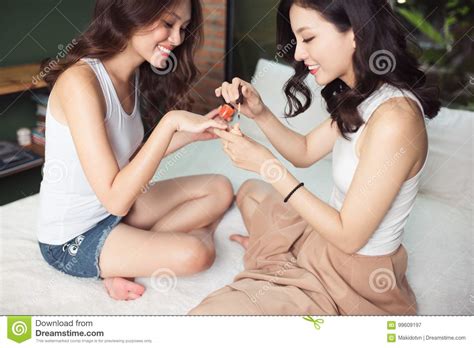 due donne asiatiche nella camera da letto sul letto dipingono i loro chiodi e immagine stock