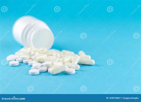 close up white pill bottle with spilled out pills and capsules on blue background with copy