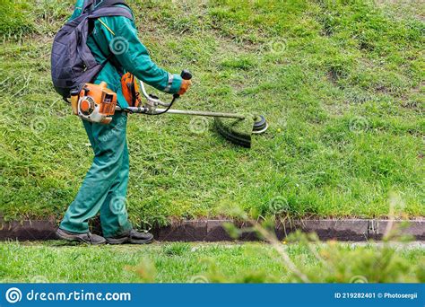 A Worker Mows Green Grass On A Hill With A Petrol Trimmer Stock Image