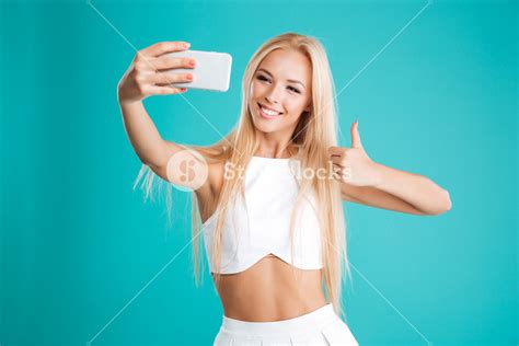 Portrait Of A Happy Smiling Girl Taking Selfie And Showing Thumb Up Gesture Isolated On The Blue