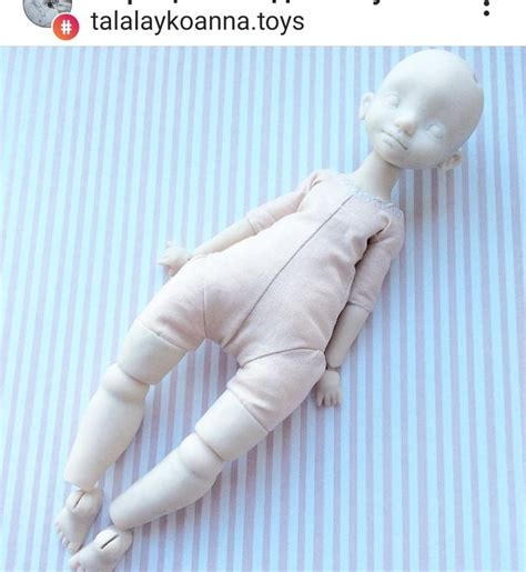 A Doll Laying On Top Of A Blue And White Striped Bed Sheet With Text