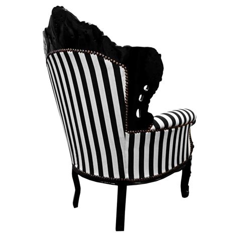White armchair in front of black wall. Big baroque style armchair striped black & white & black wood