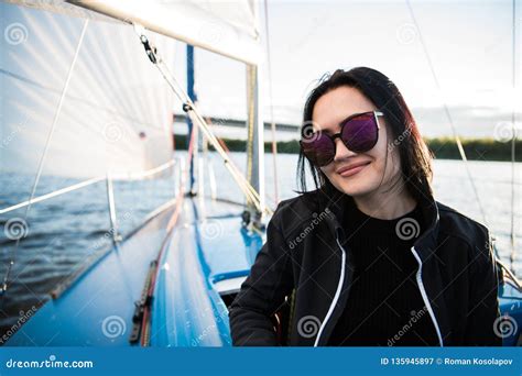 Young Smiling Dark Haired Woman Wearing Sunglasses Sitting On A Board