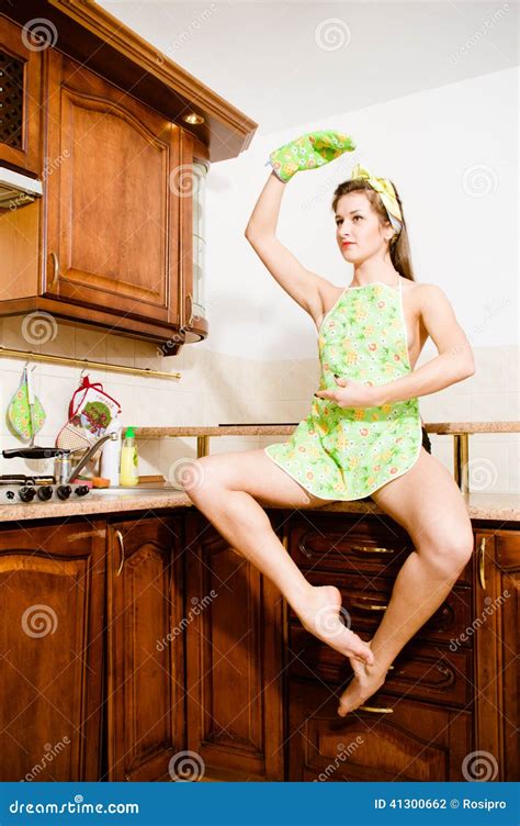 Dancing Girl Sitting On The Table In The Kitchen Apron Hand Up Looking