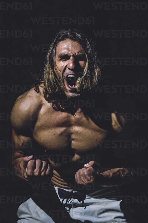 Shirtless Man Screaming While Standing In Darkroom At Gym Stock Photo
