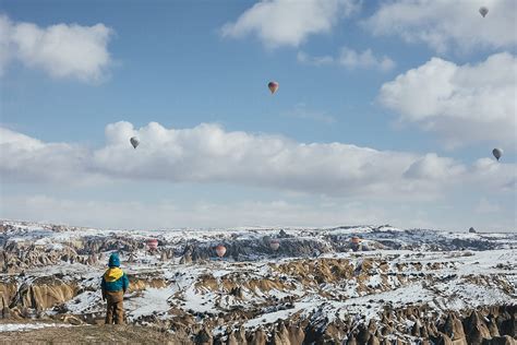 Toddler In Winter Clothes Overlooking Snowcovered Cappadocia With Hot