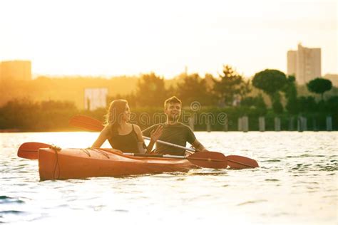 Confident Young Couple Kayaking On River Together With Sunset On The