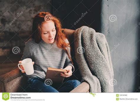 Happy Redhead Woman Relaxing At Home In Cozy Winter Or Autumn Weekend With Book And Cup Of Hot