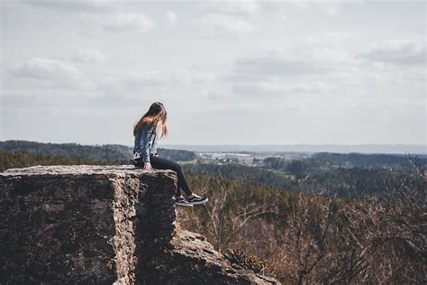 hd wallpaper woman sitting on cliff s edge overlooking forest during daytime wallpaper flare