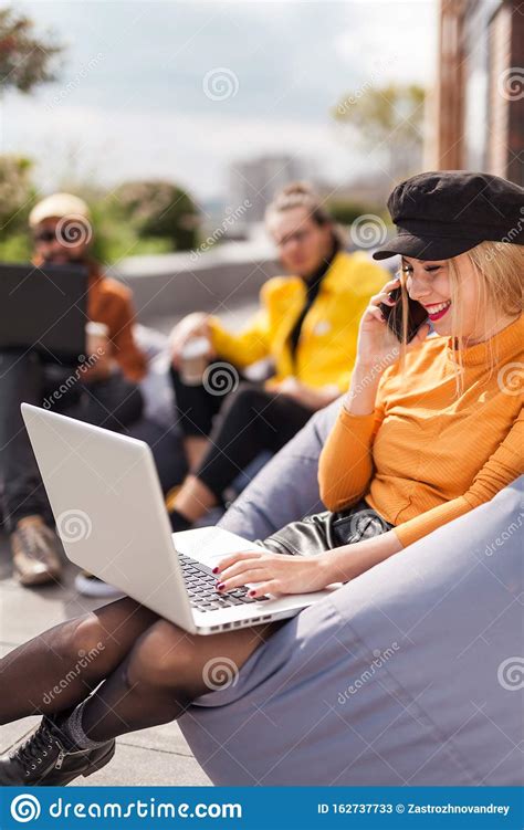 Woman Sitting On Bean Bag Using Laptop And Phone Stock Image Image