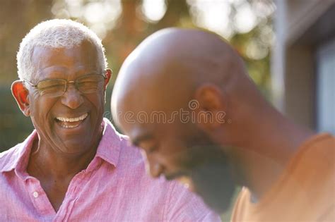 Senior Father Talking And Laughing With Adult Son In Garden At Home