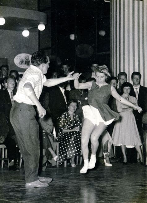 An Old Photo Of Two People Dancing In Front Of A Group Of People With Their Arms Around Each Other