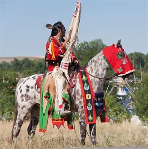 A Traditionally Dressed Crow Indian Man Rides An Appaloosa Horse During
