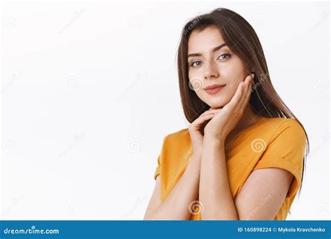 sensual attractive sassy brunette woman in yellow t shirt gently touching clear skin smiling