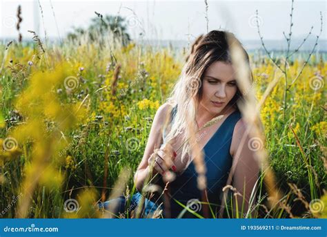A Beautiful Blonde Woman In A Blue Long Dress Sitting In A Field In Flowers The Concept Of