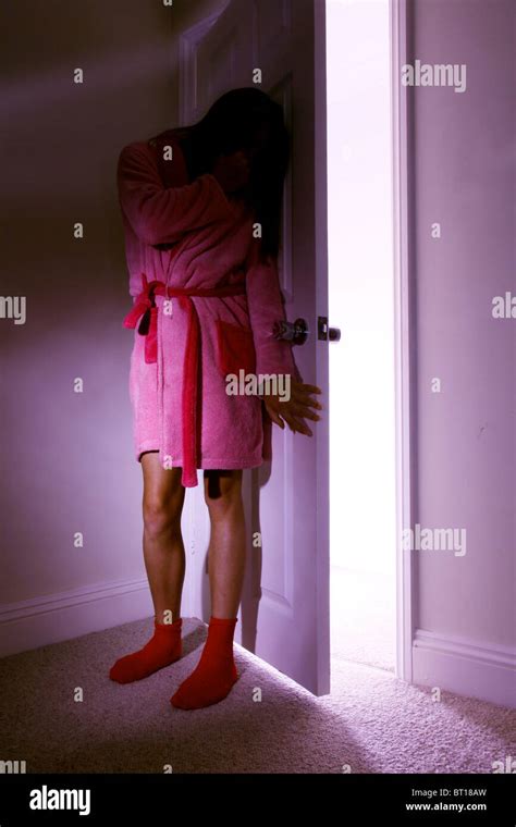Young Girl Wearing A Dressing Gown Hiding Behind A Bedroom Door Stock