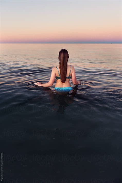 Girl Viewed From Behind Standing In Calm Water At The Beach At Sunset By Stocksy Contributor