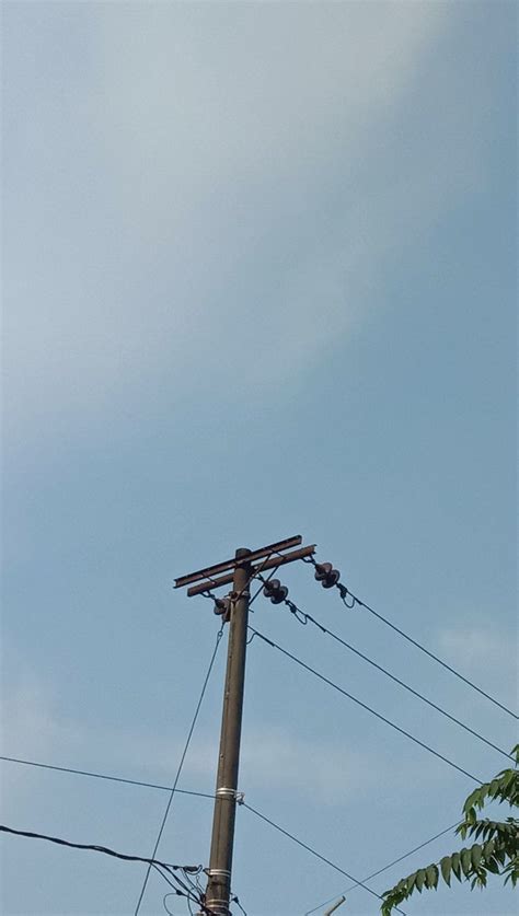 An Airplane Is Flying High In The Sky Above Power Lines And Telephone Poles With Wires Attached
