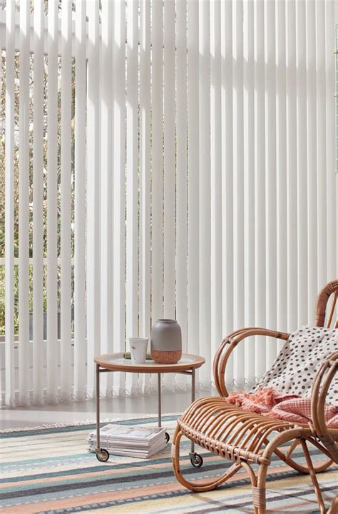 A Wicker Chair Sitting In Front Of A Window With White Vertical Blinds