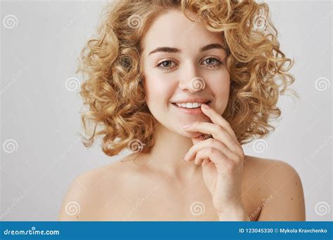 Studio Shot Of Attractive Curly Haired Blonde Smiling And Touching Lip