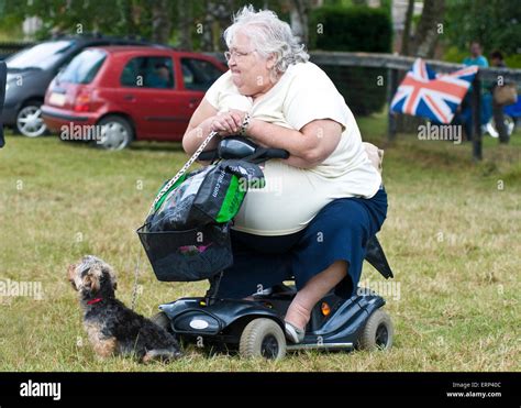 A Larger Lady Sits On Her Mobility Scooter With Her Pet Dog Stock Photo