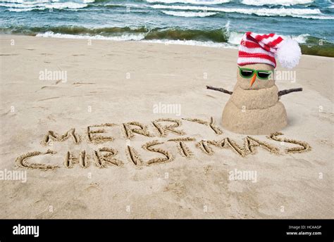 Merry Christmas In Beach Sand With Sandy Snowman With Hat Stock Photo