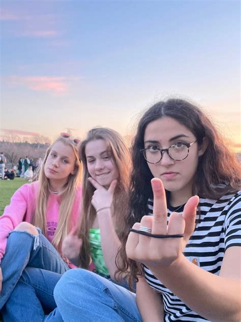 Three Girls Sitting On The Grass With Their Fingers In The Air And One
