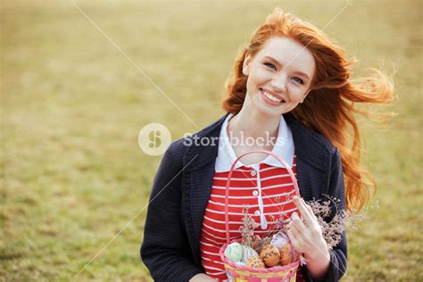 portrait of a smiling red head girl with long hair holding easter picnic basket with eggs and