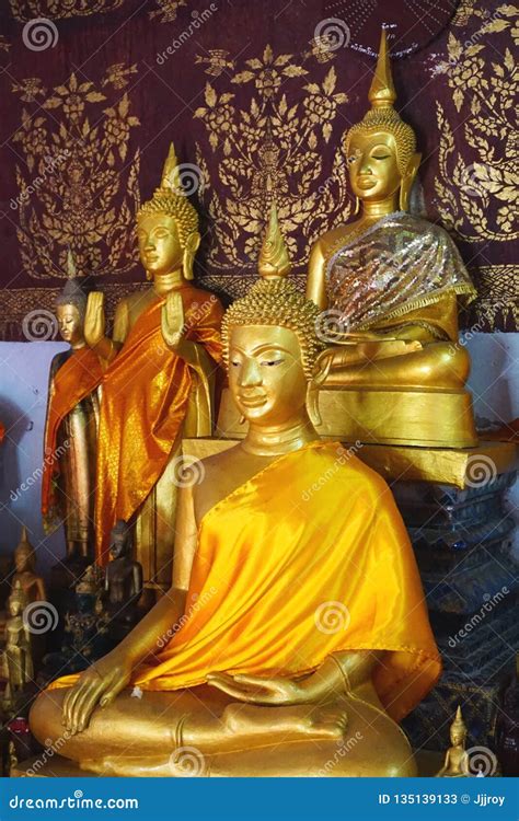 Trio Of Golden Buddha Statues With Colorful Robes In A Temple In Laos