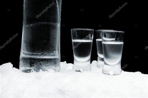 Bottle Of Vodka With Glasses Standing On Ice On Black Background Stock