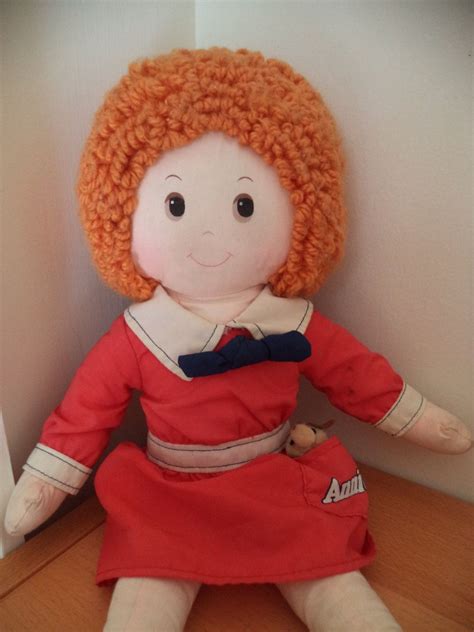 An Orange Haired Doll Sitting On Top Of A Wooden Table Next To A White Wall