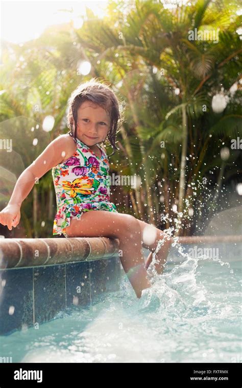 Girl Wearing Swimming Costume Sitting On Sunlit Poolside Splashing