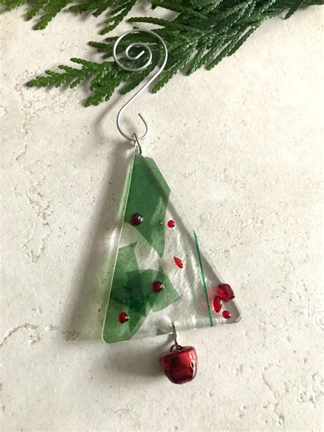 A Glass Christmas Tree Ornament Hanging From A Pine Branch With Red Berries On It