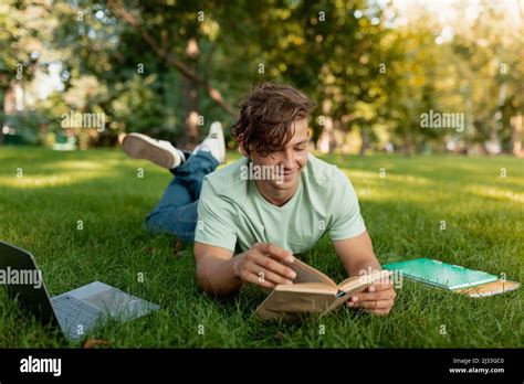 Cheerful Caucasian Student Guy Reading Book Outdoors Preparing For