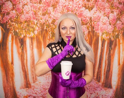 Charming Plump Blonde Woman In A Purple Corset With Long Gloves Holds A Paper Cup Of Takeaway