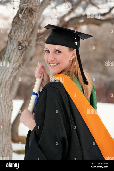 Smiling Blond Woman Holding Diploma In Graduation Cap And Gown Outdoors